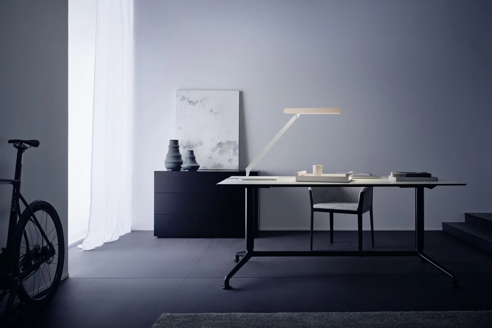 Minimalist office interior with desk, chair, lamp, artwork, and a bicycle.